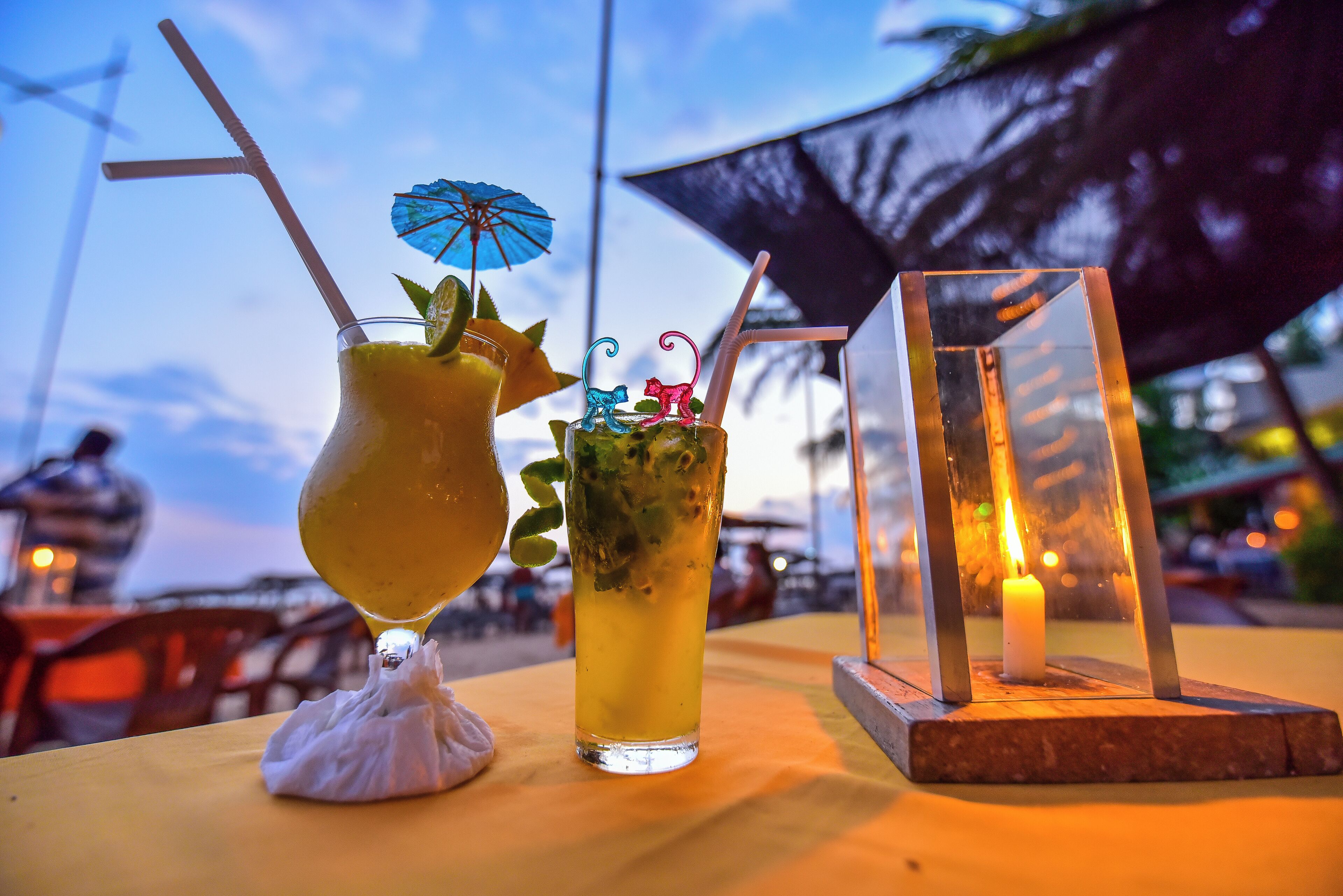 Two drinks on a table with a candle and a blue umbrella.