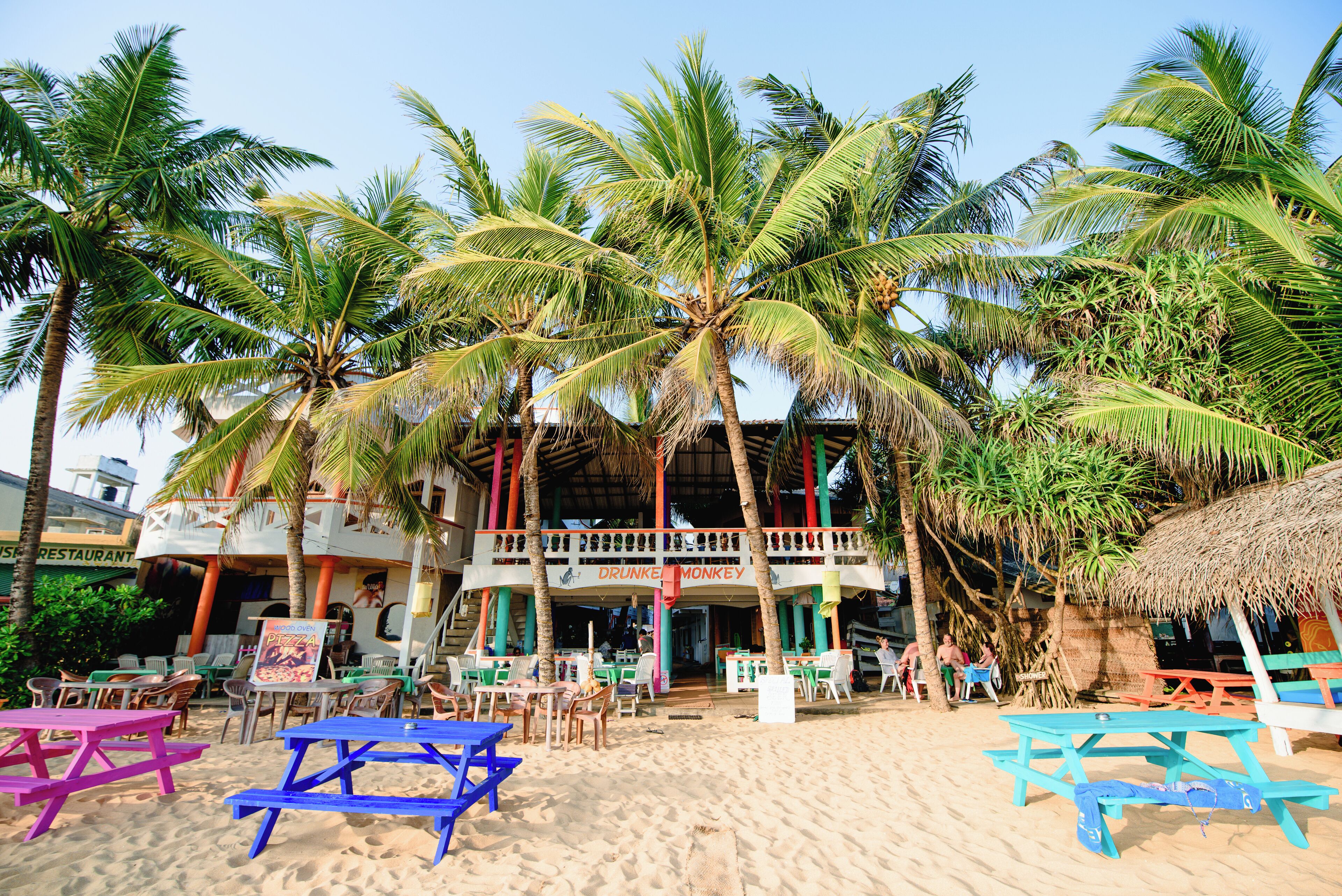 A beachside restaurant with outdoor seating and palm trees.