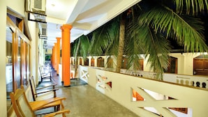 Pasillo de hotel con sillas de madera, palmeras y barandilla blanca.