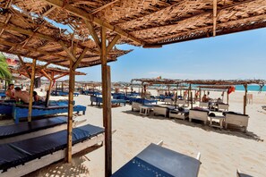 A beachside area with thatched umbrellas and lounge chairs, some with blue cushions. - International Beach Hotel and Restaurant (Hikkaduwa)