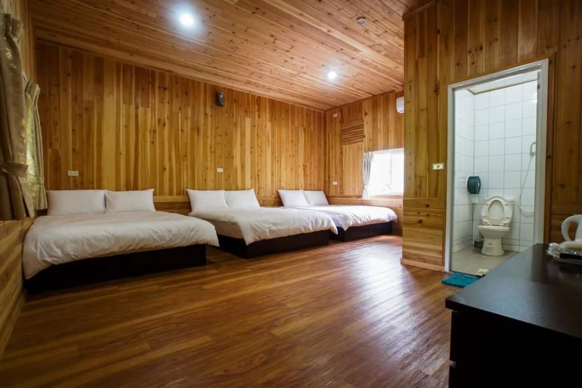 Habitació amb panells de fusta, tres llits, terra de fusta i un bany amb vàter i rentapans.