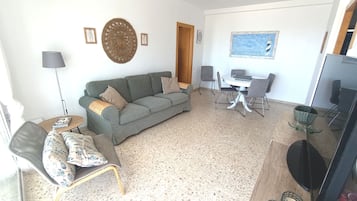 Un salon comprenant un canapé, des fauteuils, une table à manger, un téléviseur et un mur orné d’un tableau encadré.