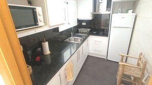 Una cucina con mobili bianchi, un piano di lavoro nero, un forno a microonde, un lavello, una stufa e un frigorifero.