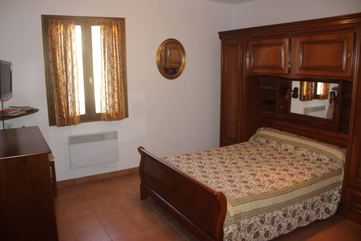 Une chambre à coucher avec un lit en bois, une commode, un miroir et une fenêtre avec des rideaux.
