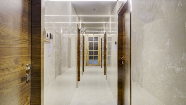 A hallway with wooden doors, a clock, and a blue-framed door at the end. - Hotel Rooms Dadar (Mumbai)