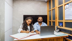 A hotel reception desk with a laptop, a telephone, and a printed document on the wall. - Hotel Rooms Dadar (Mumbai)