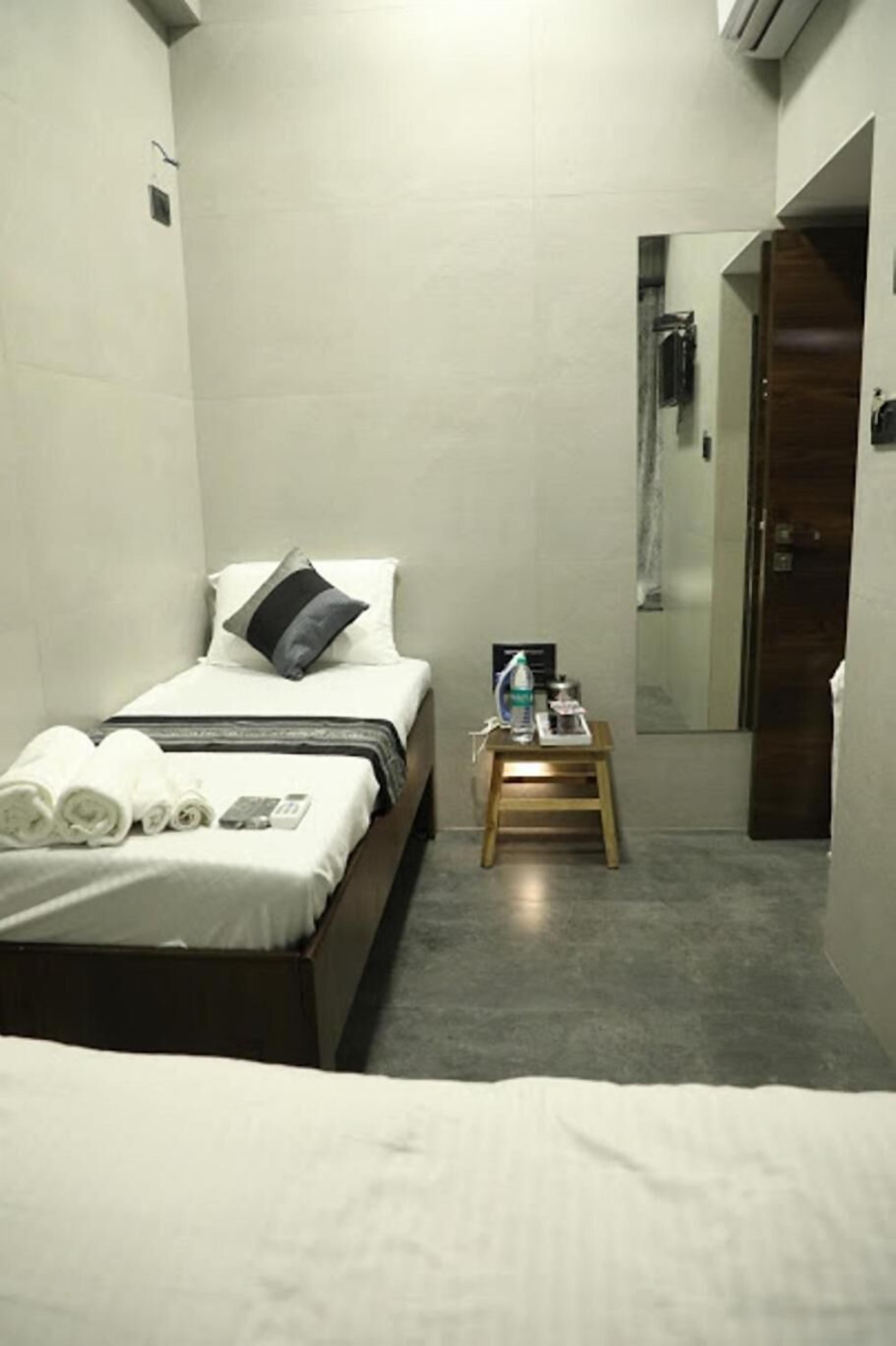 A small, modern hotel room with a single bed, a bedside table with a water bottle, and a mirror on the wall.