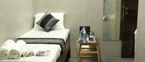 A small, modern hotel room with a single bed, a bedside table with a water bottle, and a mirror on the wall.