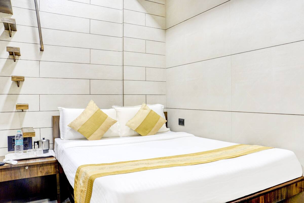 A hotel room with a large bed, a wooden nightstand, a mirror, and a wall-mounted light fixture.