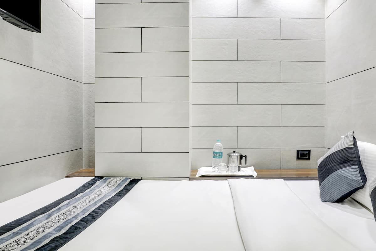 A hotel room with a bed, pillows, a water bottle, and a coffee maker on a small table.