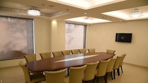 A conference room with a long table, eight chairs, a flat-screen TV, and large windows with blinds. - Hotel Mandarin Square (Dera Bassi)