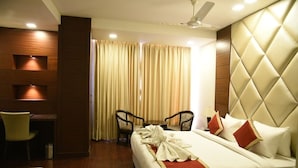A hotel room with a bed, two chairs, a desk, and a ceiling fan. - Hotel Mandarin Square (Dera Bassi)