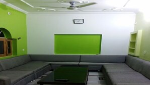 A living room with a sectional sofa, a coffee table, a green accent wall, and a ceiling fan. - Hotel Shanti (Gaya)