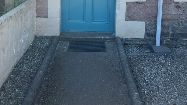 A blue door with a brass mail slot, set in a stone and plaster wall with a number plate.