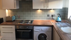 A compact kitchen with a built-in oven, a dishwasher, a washing machine, a toaster, and a kettle.