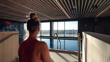A woman in a red swimsuit standing by a pool with a view of a cityscape through large windows.
