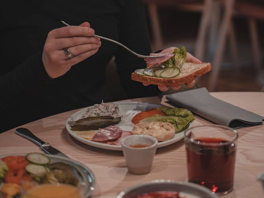 A person sitting at a table with a plate of food, a glass of drink, and a knife and fork.