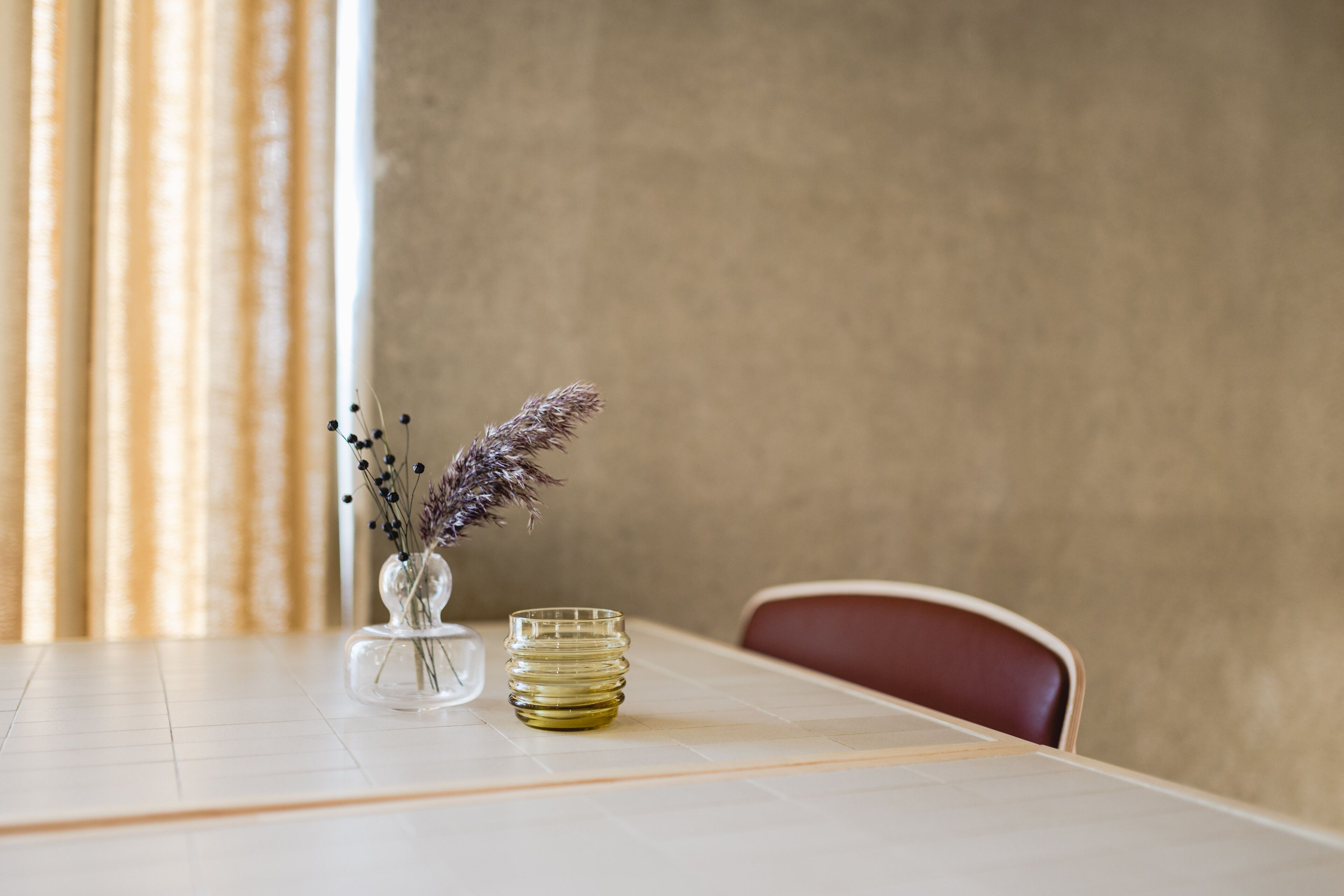 A dining table with a vase of dried flowers and a glass candle.