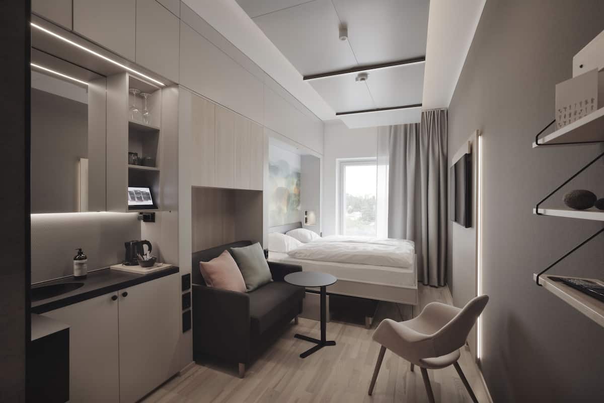 A modern hotel room with a kitchenette, a sofa, a small table, and a bed.