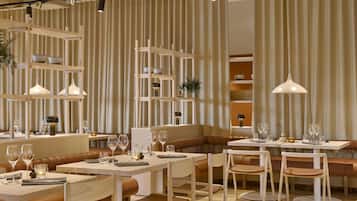 Um restaurante moderno com mesas e bancos de madeira, iluminação pendente e um painel de cortinas listradas.