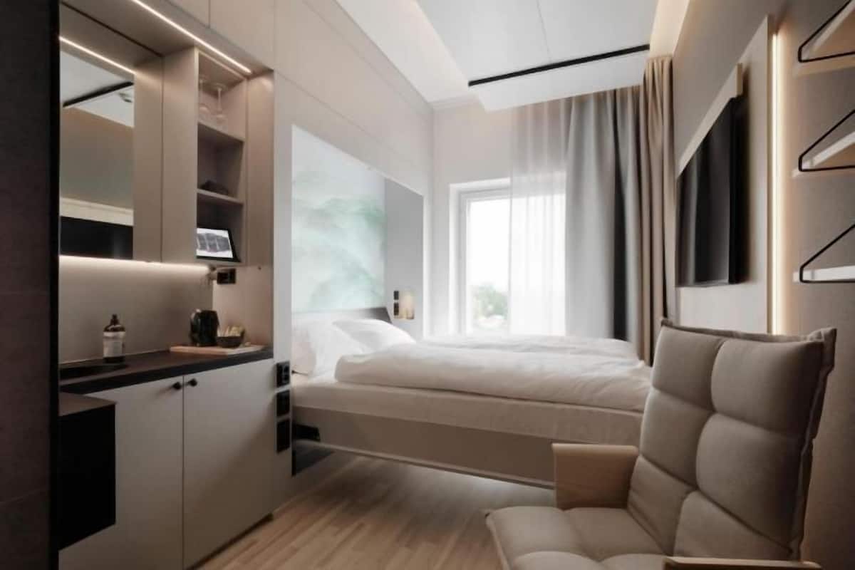 A modern bedroom with a bed, a chair, a desk, and a large window.