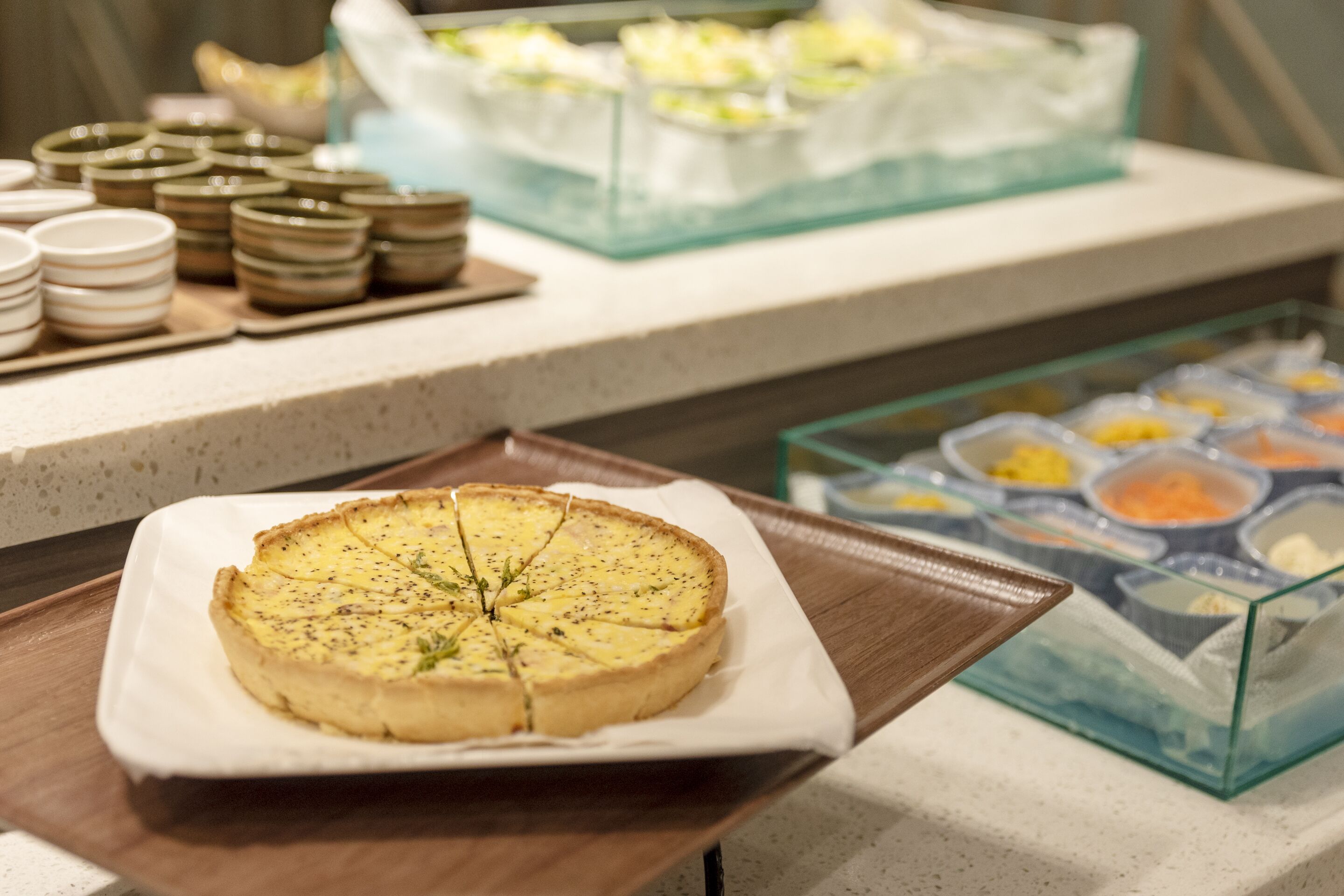 A buffet with various dishes, including a quiche on a white plate, arranged on a counter.