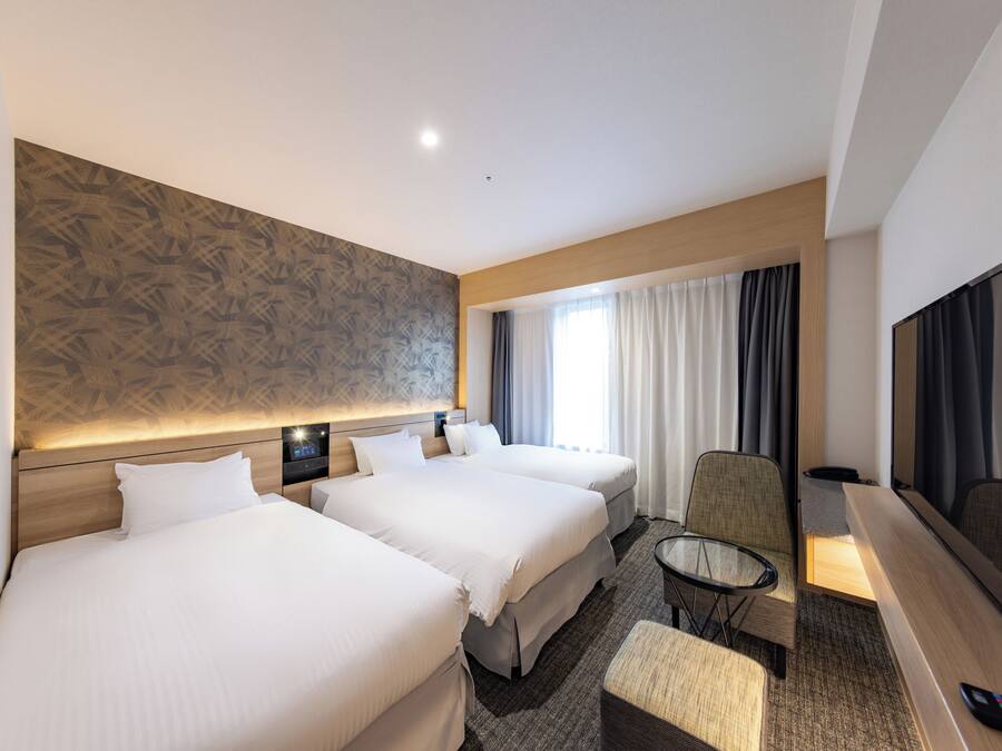 A hotel room with two beds, a TV, a small table, and a chair.