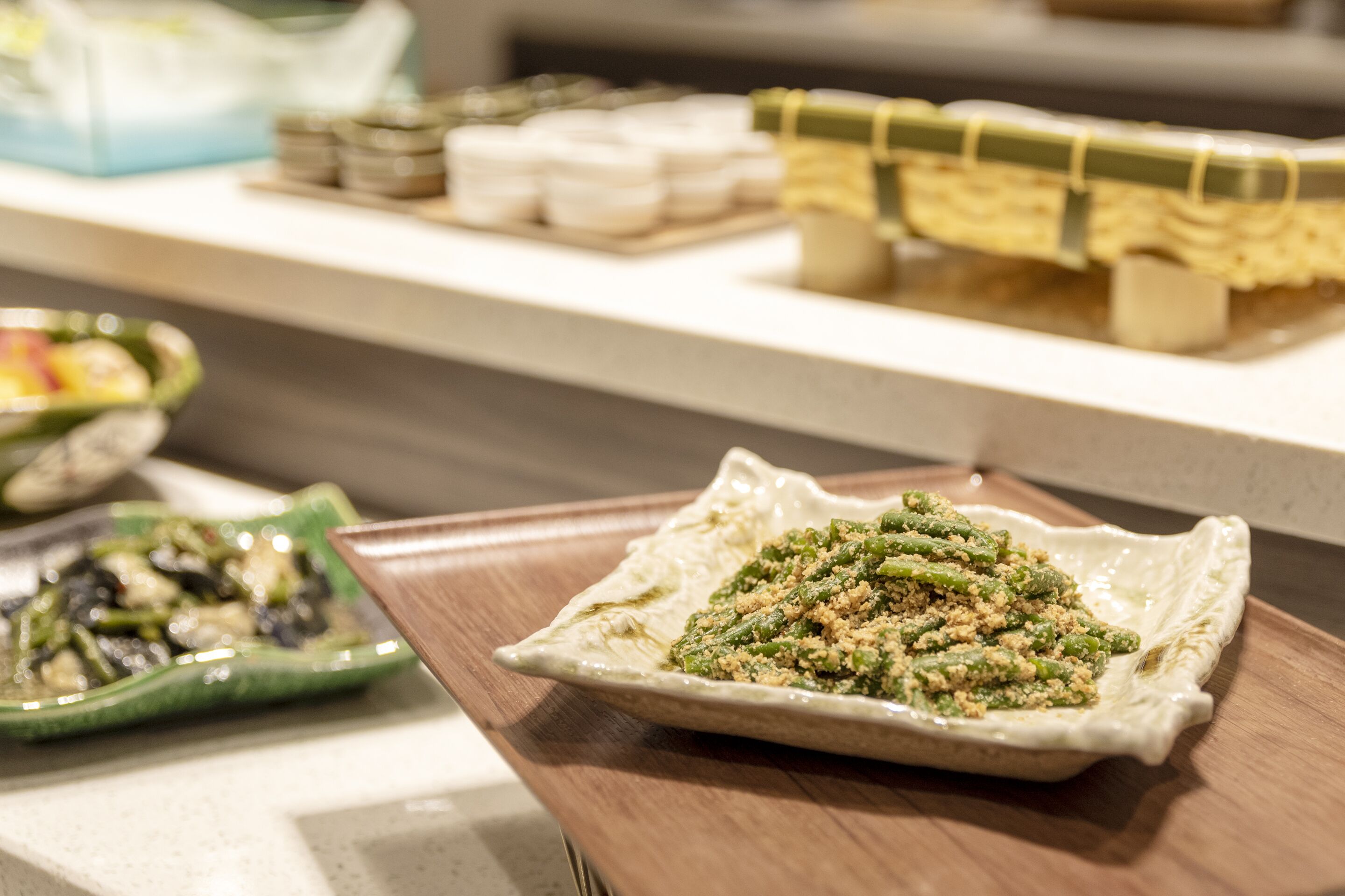 A buffet table with various dishes, including a green vegetable dish and a dish with green beans and breadcrumbs.