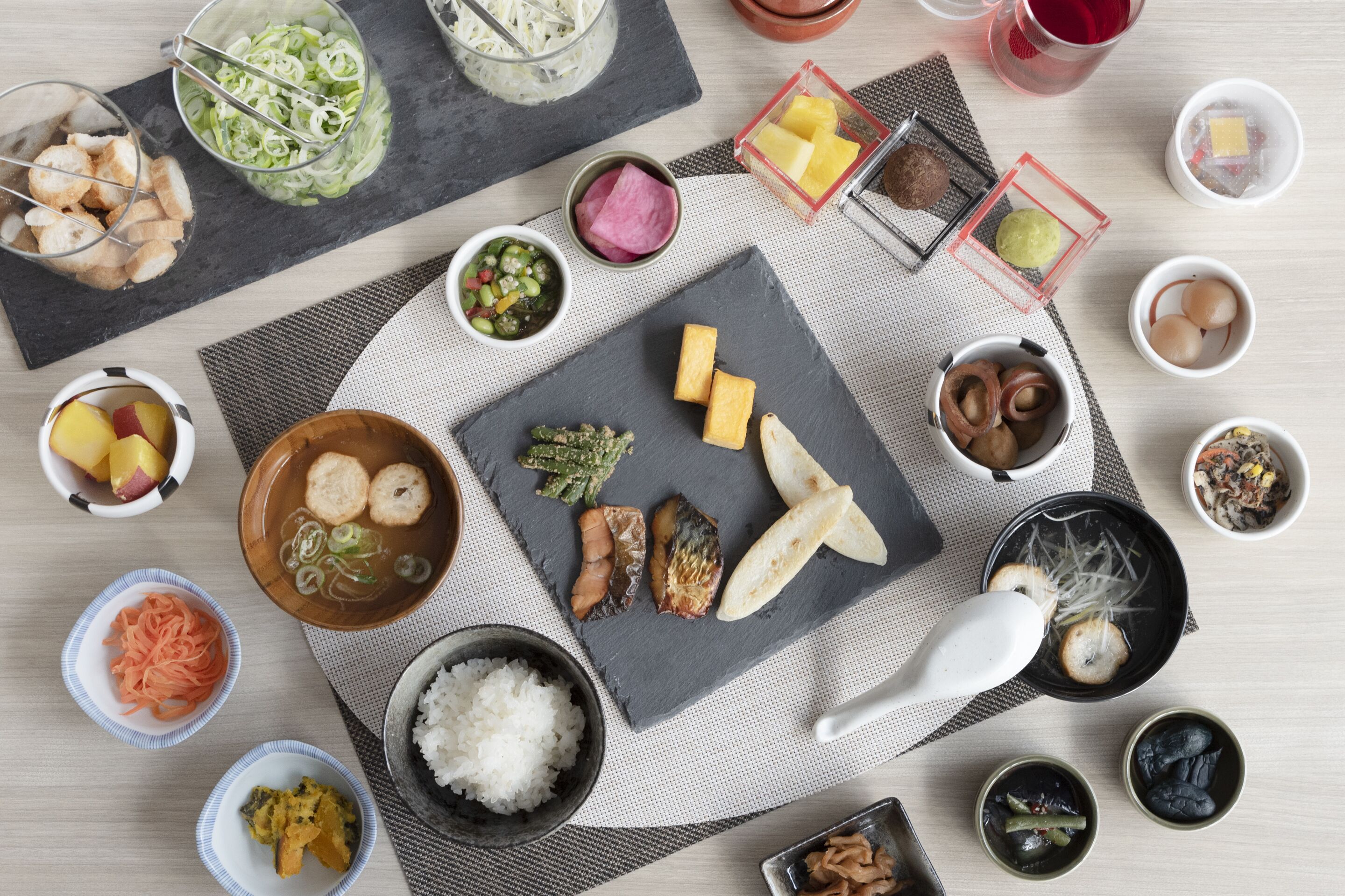 A variety of dishes and condiments arranged on a table, including a bowl of rice, a plate of fish, and several small bowls containing different sauces and vegetables.