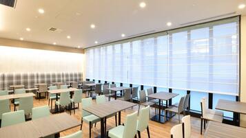 A spacious conference room with multiple tables and chairs, large windows with blinds, and ceiling vents.