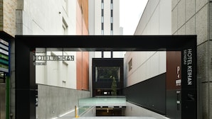 Une entrée d’hôtel moderne, dotée d’un auvent en verre, d’une enseigne indiquant l’hôtel Keihan Sendai et d’un chemin dégagé menant à l’entrée.