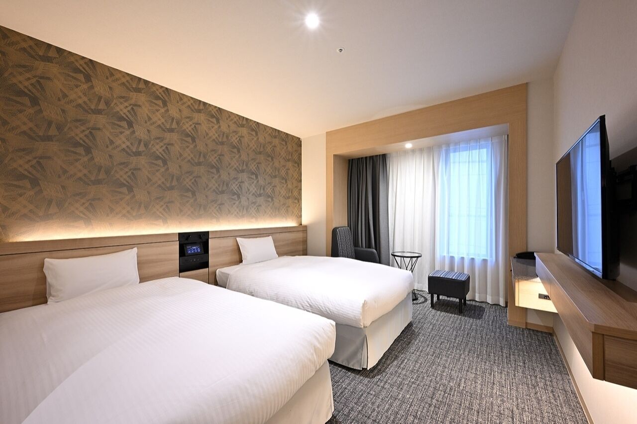 A hotel room with two beds, a television, a desk, and a small table.