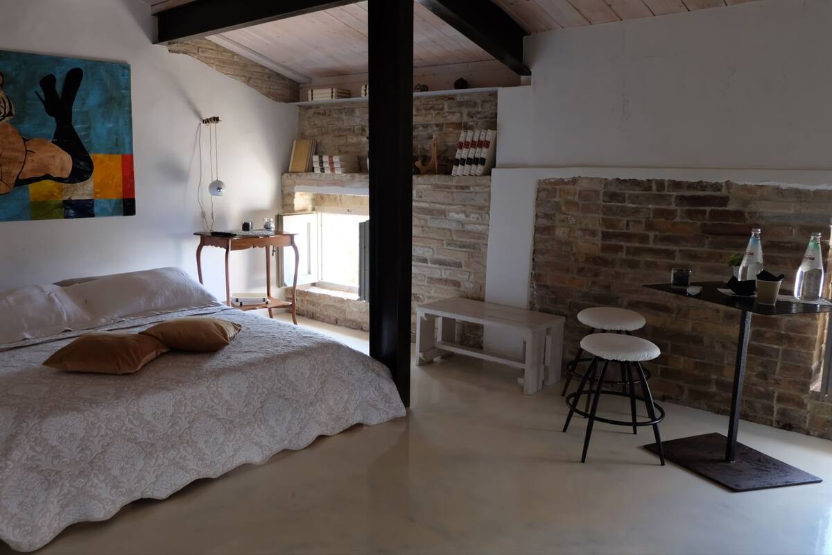 Une chambre à coucher avec un lit, un tableau, une table avec des tabourets et un mur en briques.