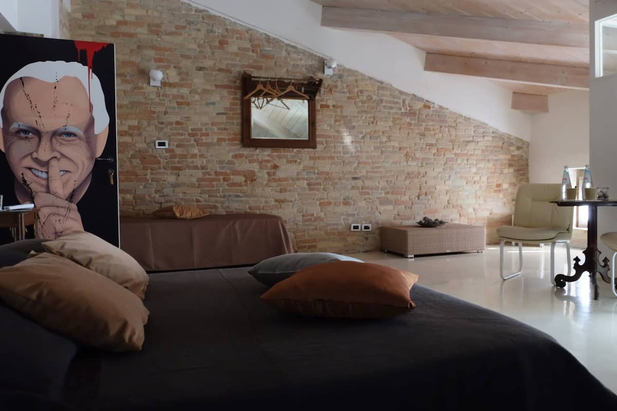 Une chambre moderne avec un mur en briques, un lit agrémenté de plusieurs coussins, une petite table avec des bouteilles et une chaise.