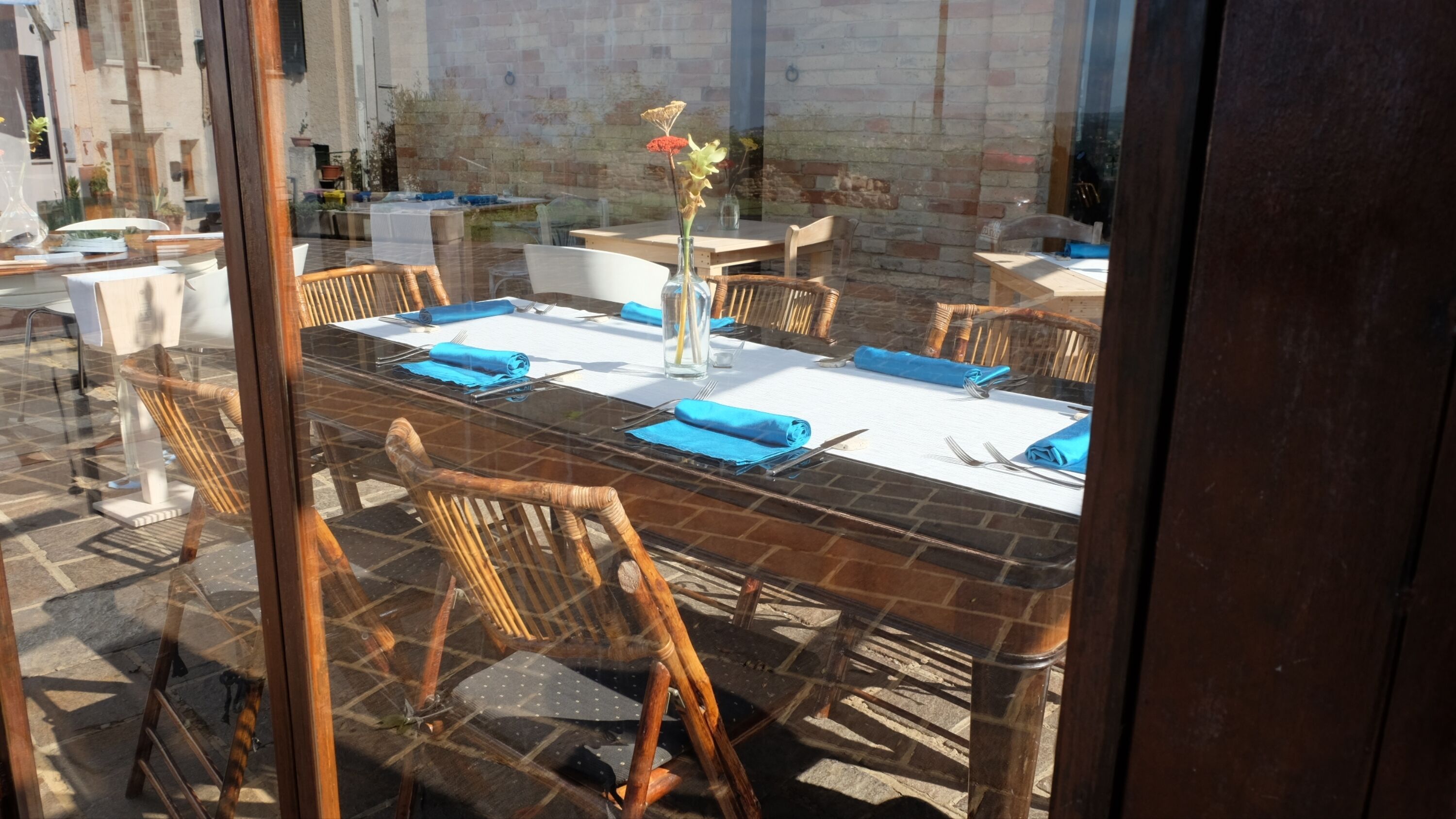A dining area with a glass table, blue napkins, and wicker chairs.