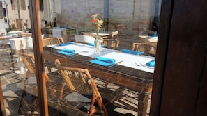 Un comedor con mesa de vidrio, servilletas azules y sillas de mimbre.