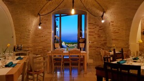 Un comedor con paredes de ladrillo, una mesa preparada para cuatro personas y vista al mar a través de un ventanal.