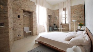 A bedroom with exposed brick walls, a large bed with white linens, a small table with a lamp, and a chair. - BR1 Cibo & Benessere (Montesilvano)