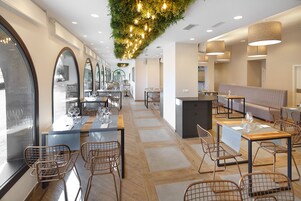Un interior de restaurante moderno con suelo de madera, sillas de metal y mesas preparadas para comer.