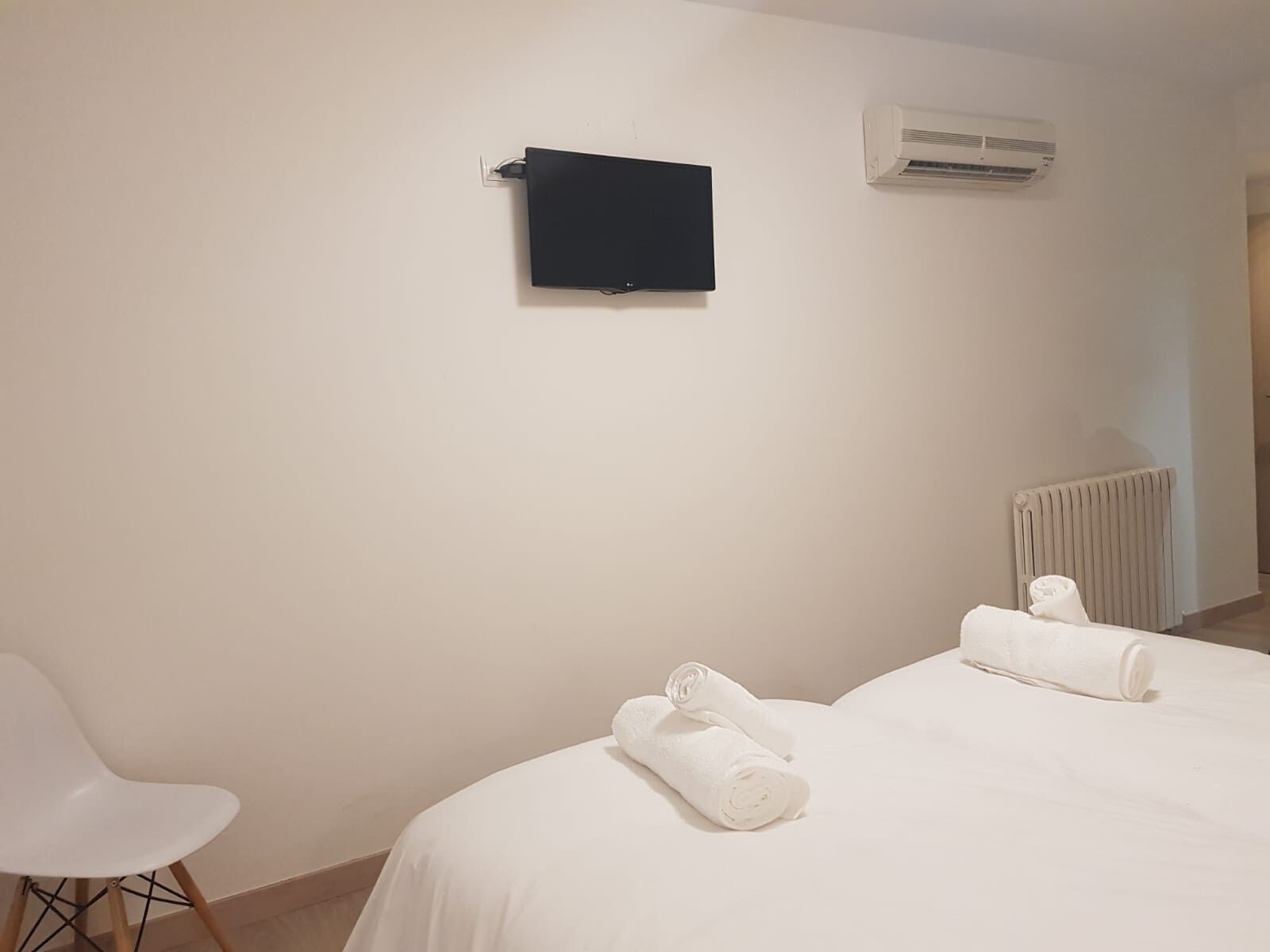 Ein Hotelzimmer mit einem Bett, zwei aufgerollten Handtüchern, einem weißen Stuhl, einer schwarzen Platte und einer Klimaanlage.