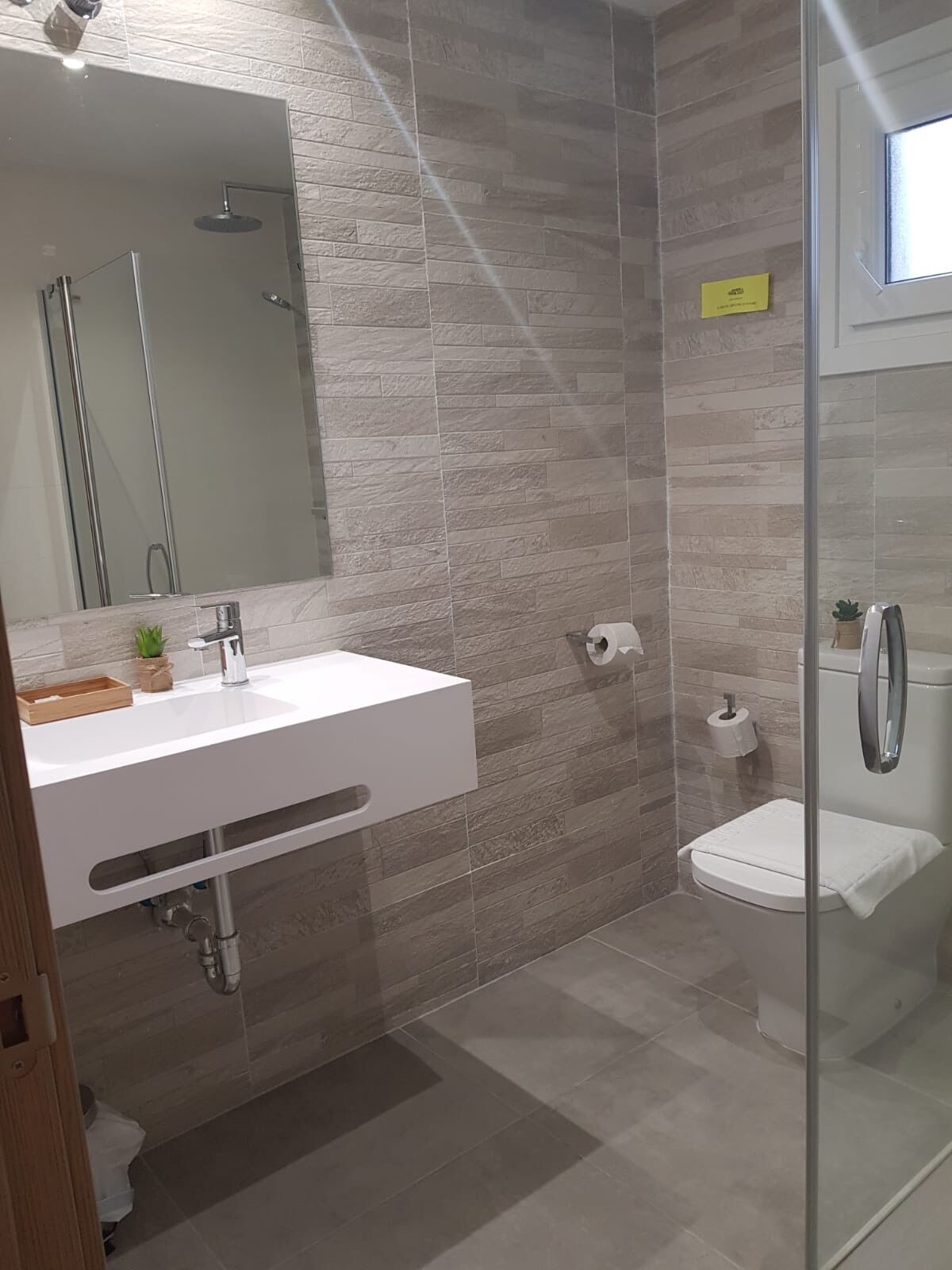 A modern bathroom with a white sink, a glass shower enclosure, and a toilet.