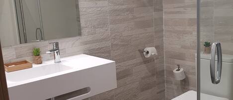 Un bany modern amb un lavabo blanc, un plat de dutxa de vidre i un vàter.