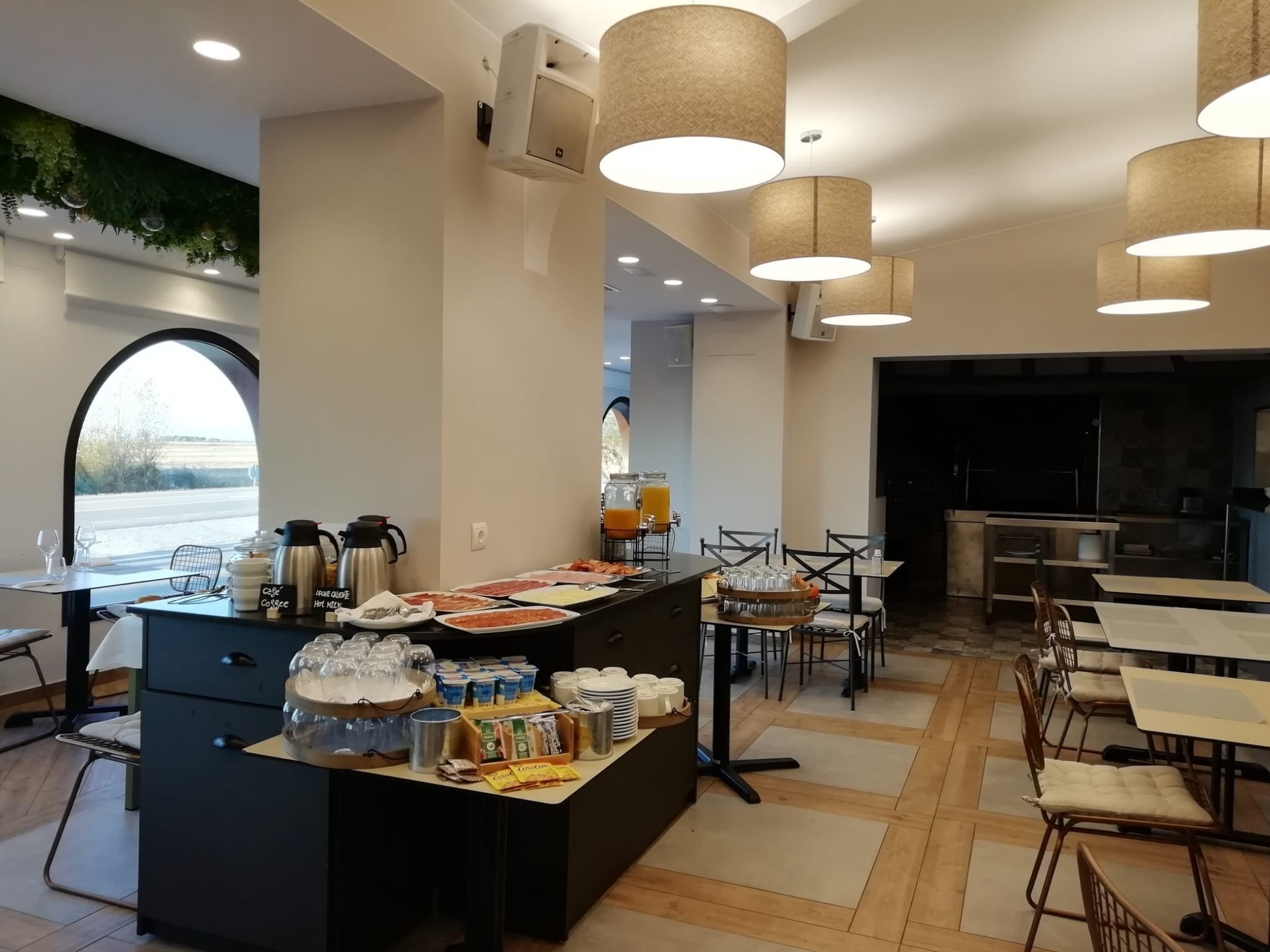 Uma área de café da manhã com serviço de buffet, incluindo diversos alimentos e bebidas, e um espaço de estar com mesas e cadeiras.