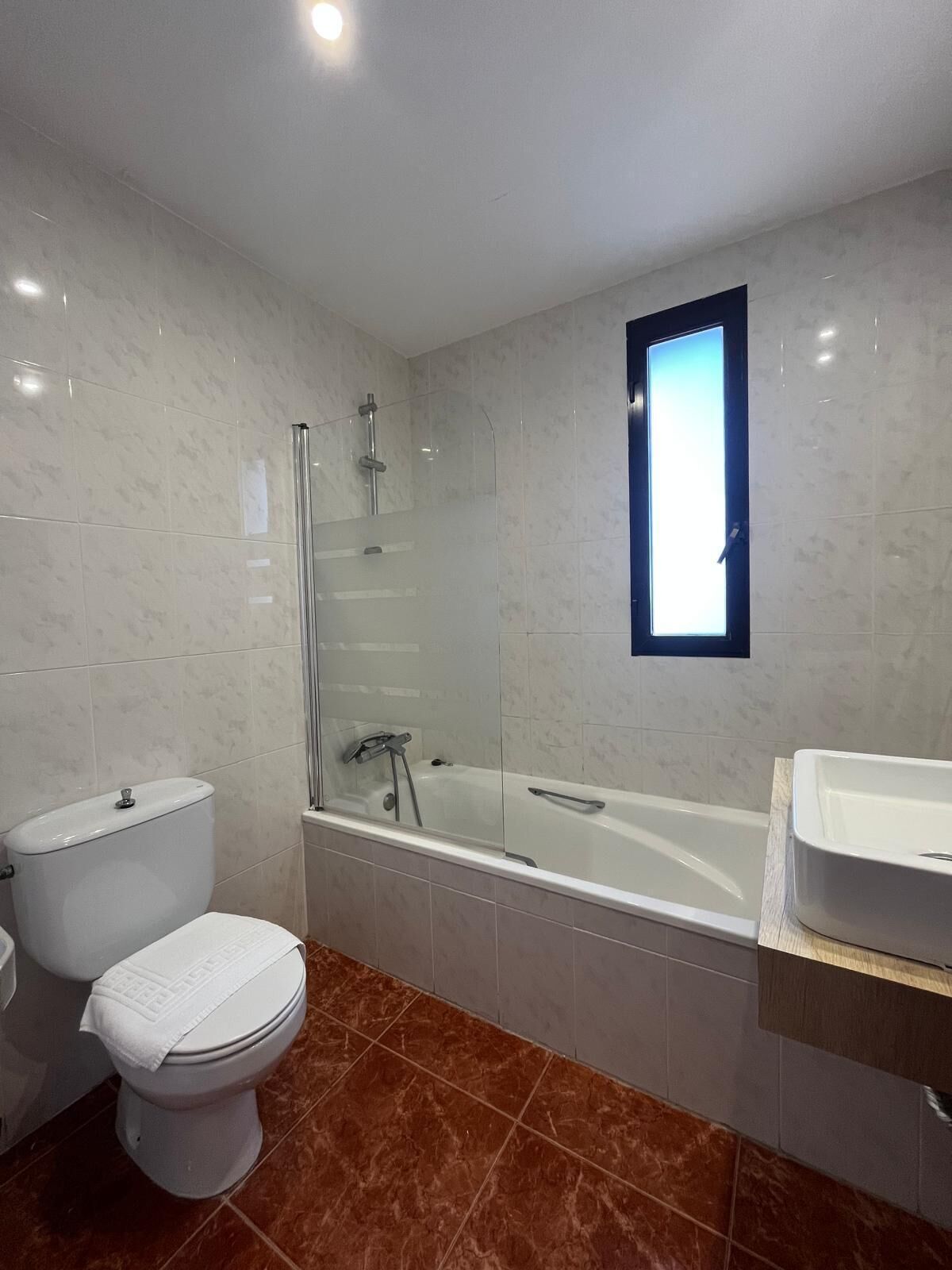A modern bathroom with a glass-enclosed shower, a standalone toilet, and a freestanding bathtub.