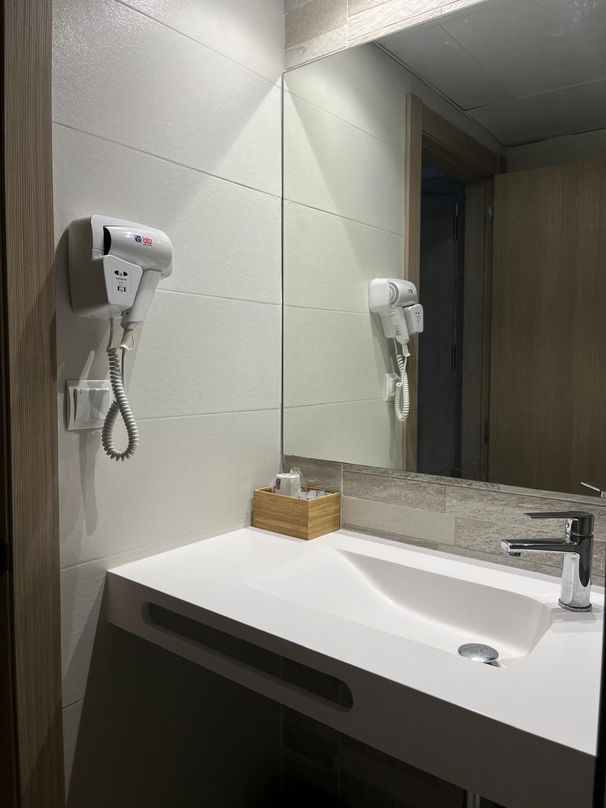 Une salle de bain avec un lavabo blanc, un miroir et deux sèche-cheveux fixés au mur.