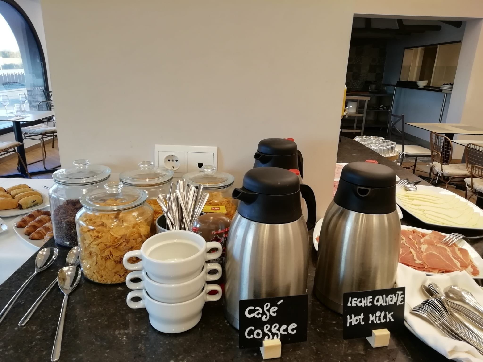 A breakfast buffet with jars of cereal, croissants, and a coffee station.