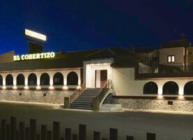 Un edificio con una señal que dice "EL COBERTIZO" de noche, con una escalera y ventanas arqueadas.