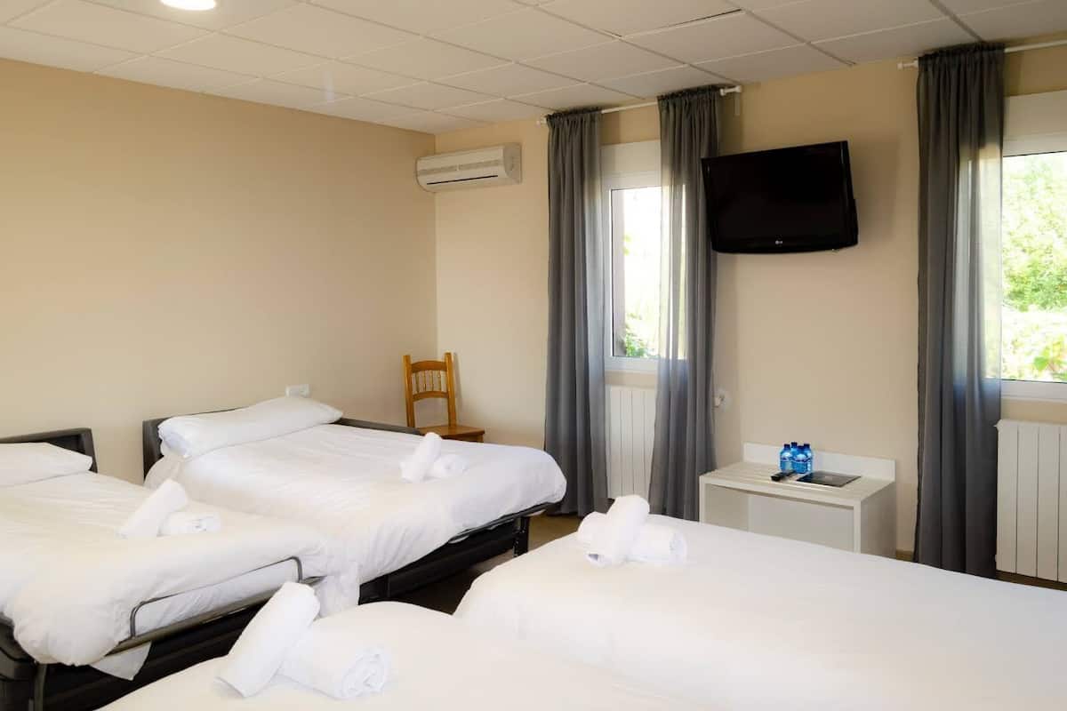 Habitación de hotel con dos camas, un televisor montado en la pared, una mesita con una botella de agua y una silla.