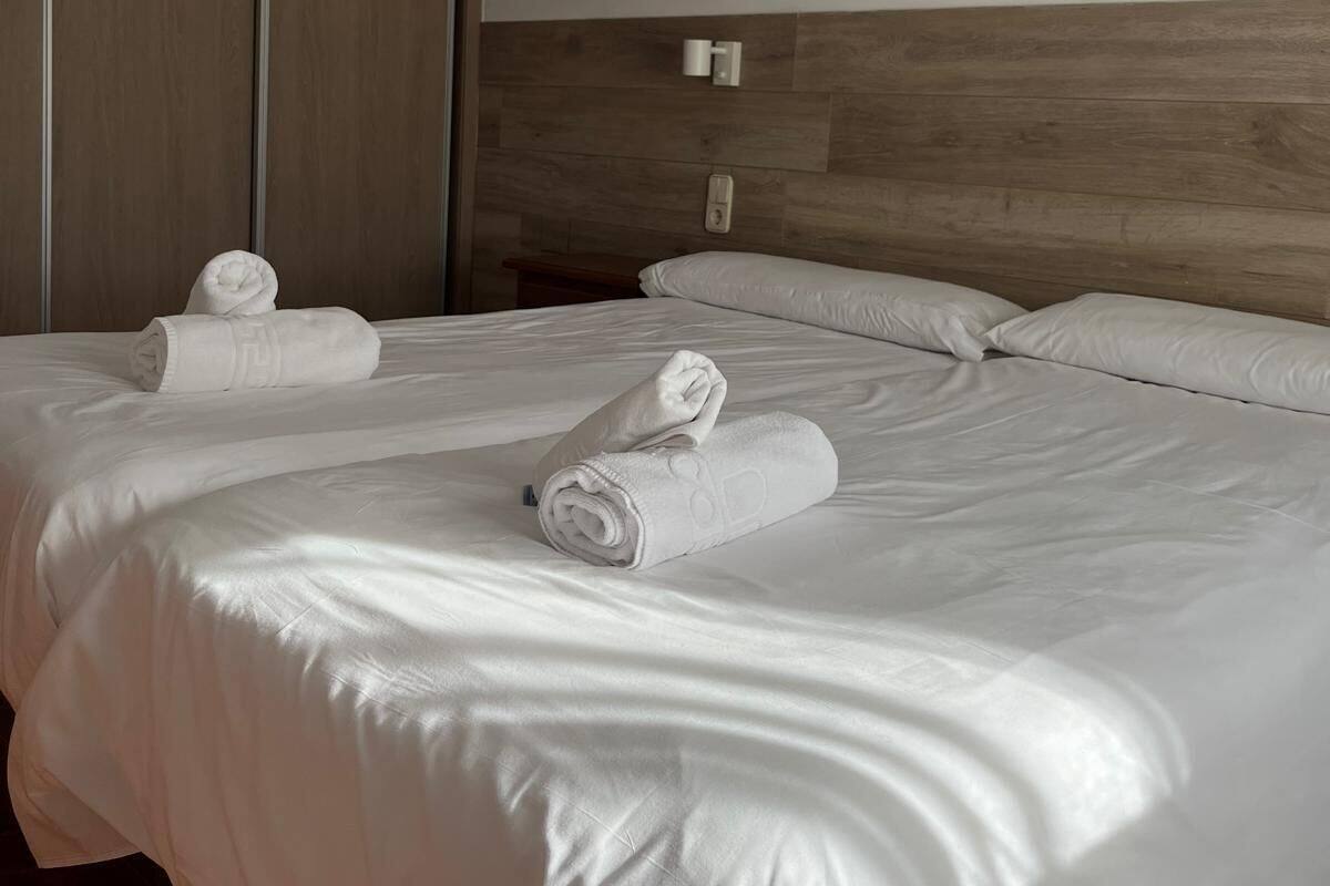 Habitación de hotel con una cama grande, dos almohadas y dos toallas enrolladas sobre la cama.