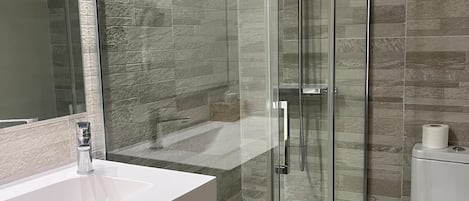 Un baño moderno con ducha de vidrio, lavamanos blanco y retrete.